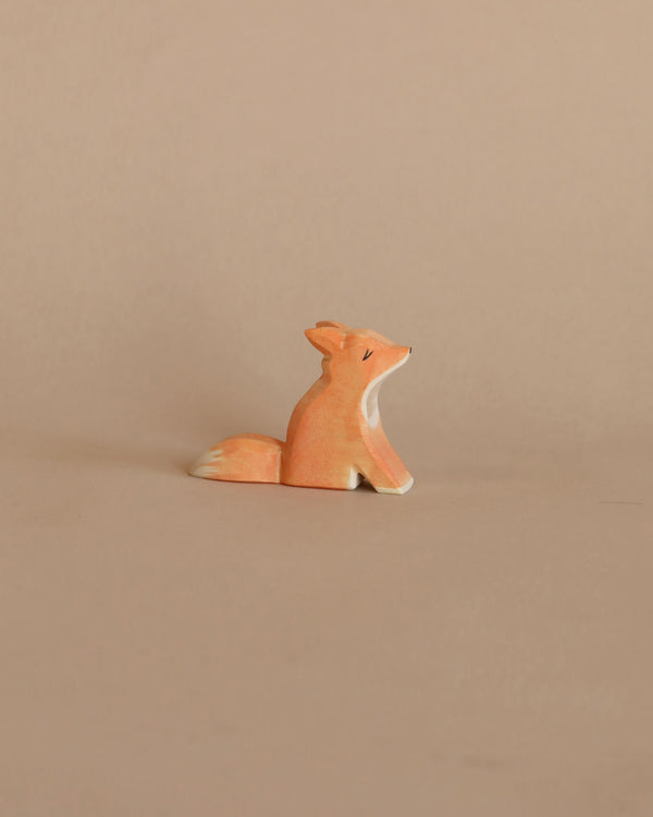A handcrafted Ostheimer Small Fox - Sitting figurine, painted orange with white details, sitting against a plain beige background.