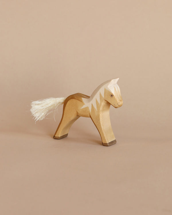 A handcrafted Ostheimer Horse with smooth, contoured edges and a white yarn tail stands on a light brown background, showcasing a simplistic and elegant design.