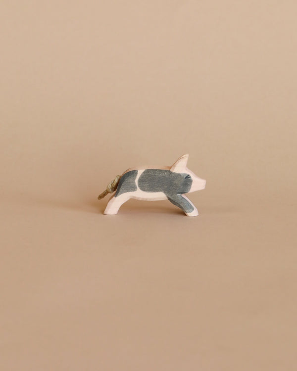 A handcrafted wooden figurine of an Ostheimer Spotted Piglet - Running mid-stride against a plain beige background. The piglet is painted realistically with detailed coloration on its body.