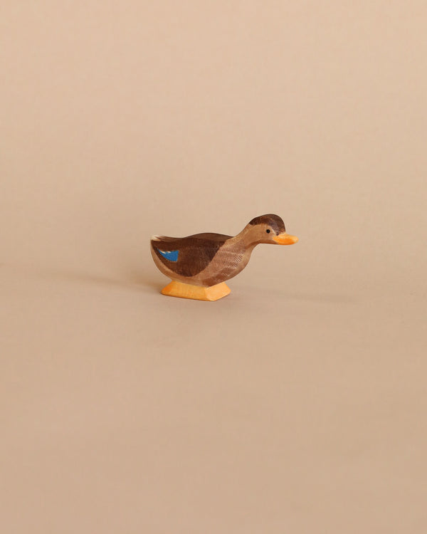 A small Ostheimer Long Neck Duck figurine with a brown body and blue accents, standing against a plain, light beige background.