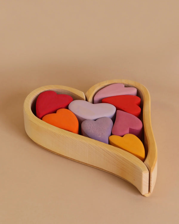 A Grimm's Red Hearts Building Blocks filled with vibrant heart-shaped building blocks in various shades, including red, pink, purple, orange, and yellow. Perfect for enhancing fine motor skills, this charming desk-toy adds a splash of color to any beige background.