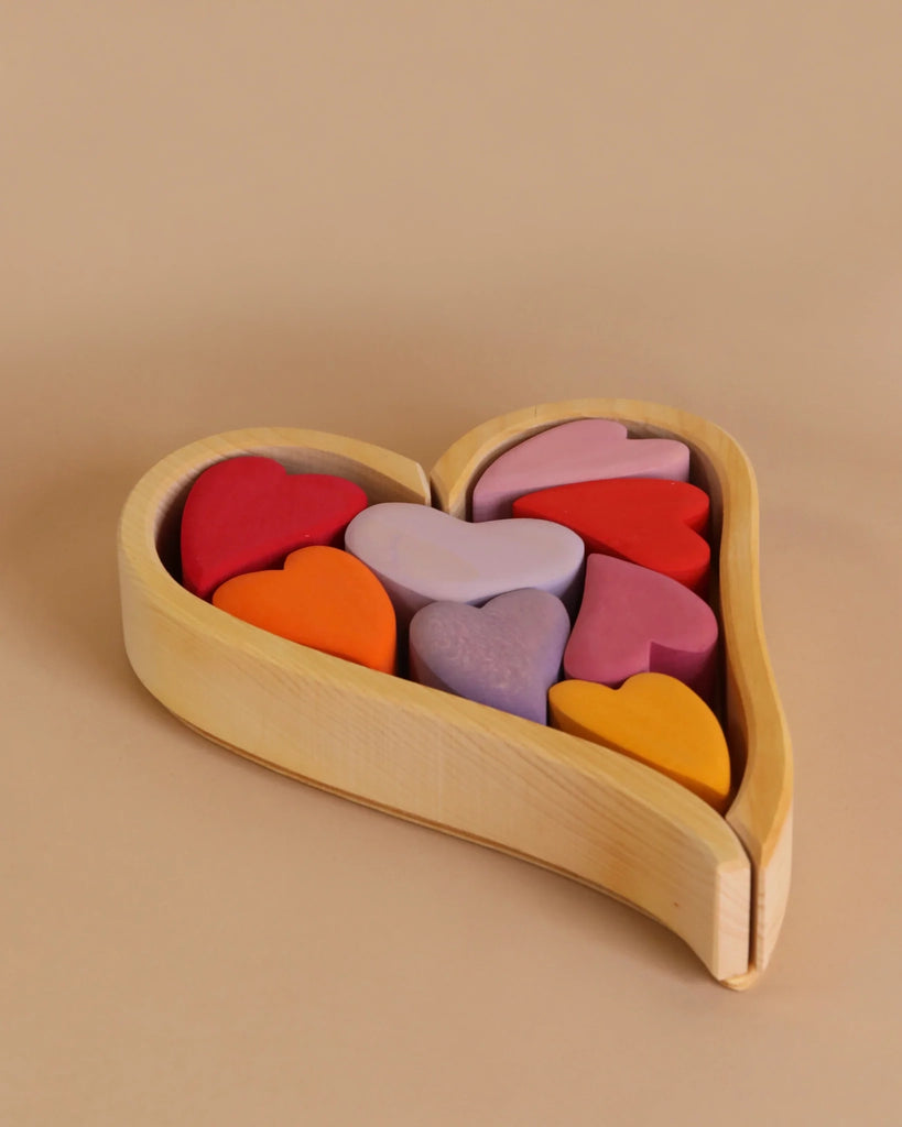 A Grimm's Red Hearts Building Blocks filled with vibrant heart-shaped building blocks in various shades, including red, pink, purple, orange, and yellow. Perfect for enhancing fine motor skills, this charming desk-toy adds a splash of color to any beige background.