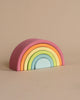 A Grimm's Rainbow Pastel Stacker, crafted from non-toxic wood, is displayed against a plain beige background. This versatile toy consists of seven arches, ranging from pink on the outermost layer to light blue on the innermost layer, resembling a charming rainbow tunnel.