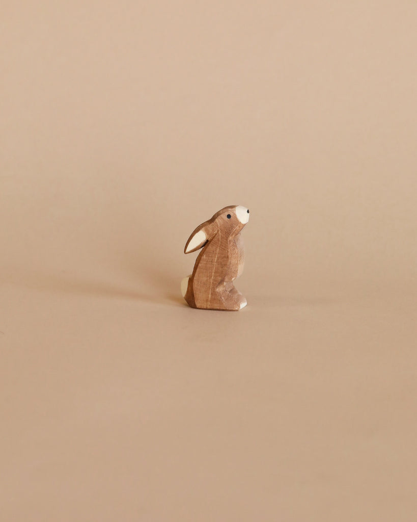 A charming brown wooden rabbit figurine from the Enchanted Woodland Farm Set sits upright on a beige surface with a matching background, capturing the handmade appeal reminiscent of classic Ostheimer wooden toys.