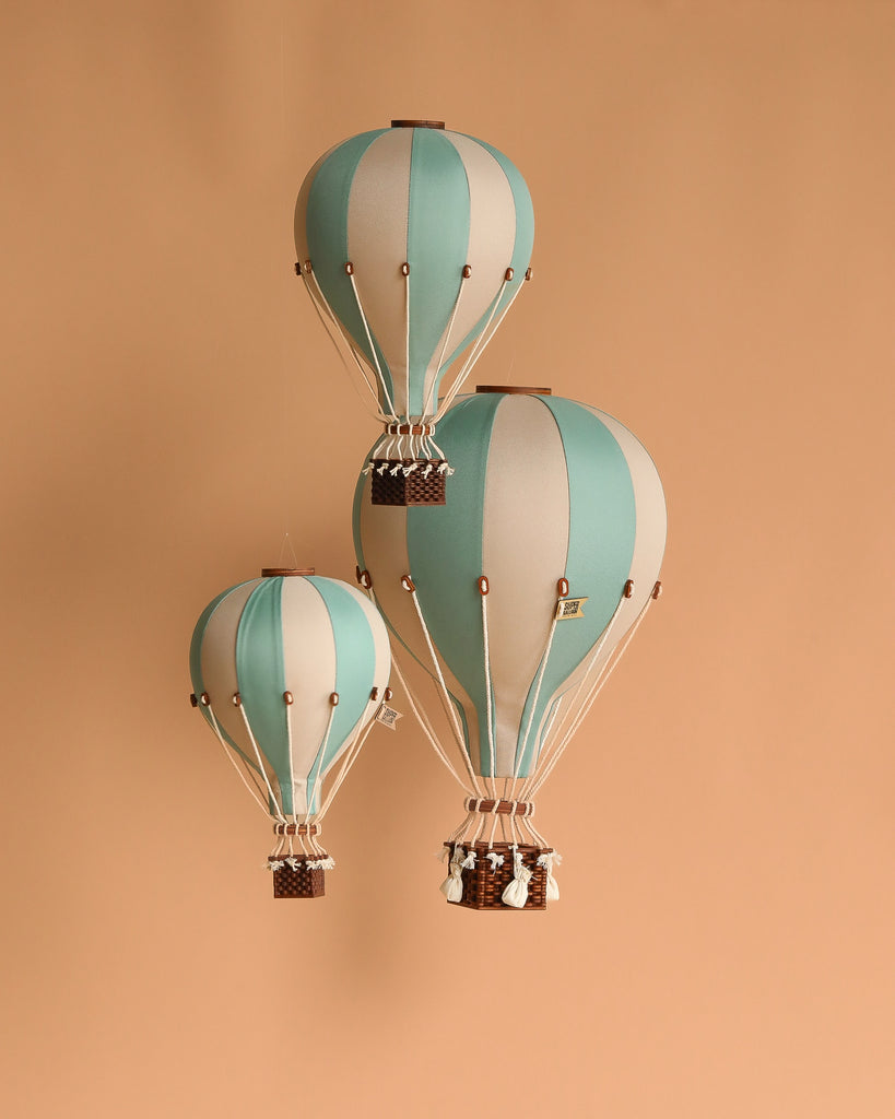 The Hot Air Balloon - Pastel Green features teal and white stripes with a small wicker basket attached by white strings, creating a charming handmade decoration ideal for a child's room.