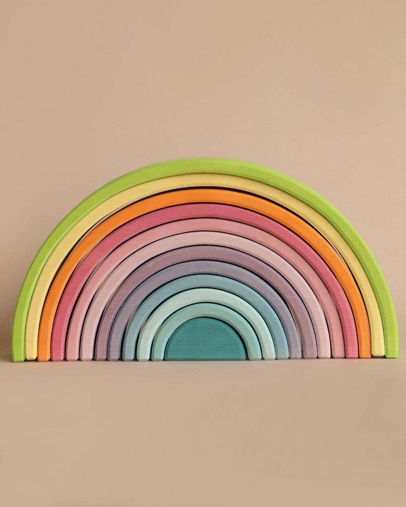 A Large Wooden Rainbow, Pastel made from non-toxic wood arranged in an orderly fan shape. Each arch is painted a different color, creating a vibrant gradient from green on the outermost arch to teal in the center, against a plain, neutral background.