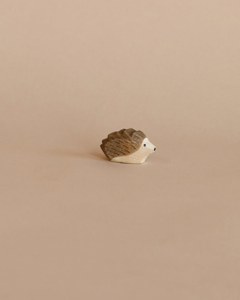 A small carved wooden hedgehog from the Enchanted Woodland Farm Set, featuring a brown back and white face inspired by Ostheimer toys, is displayed on a light beige background.