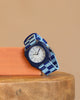 Mini Kyomo Watch - Blue Sunday - Blue Checkered stands upright on wood, leaning on an orange block with a beige background; its blue and white checkered band and blue bezel create a playful vibe for kids.