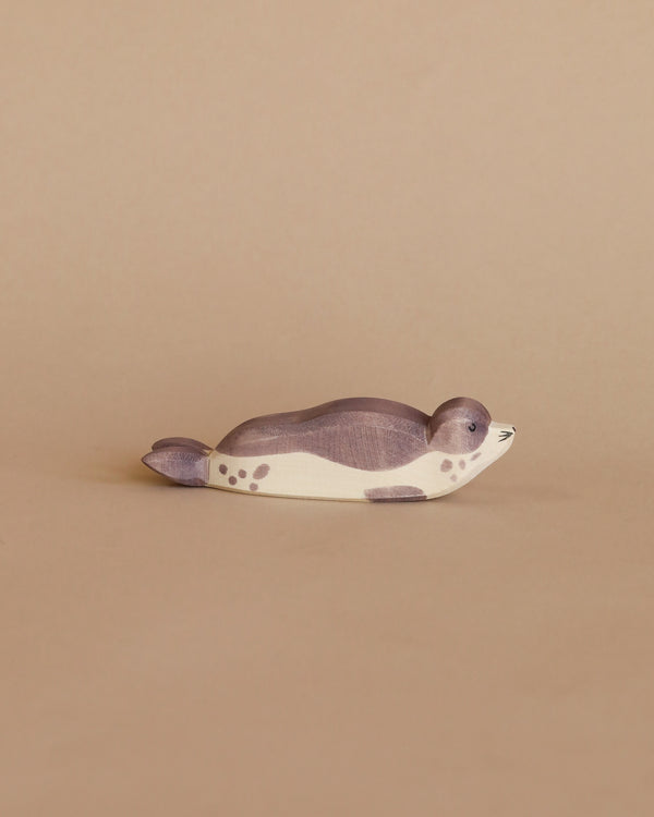 A handcrafted Ostheimer Sea Lion - Resting, painted in shades of gray and white with spots, resting on a plain beige background.