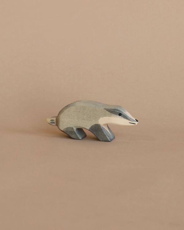 A Ostheimer Badger - Head Straight, painted in shades of grey and cream, stands against a plain light brown background. The figurine is stylized with smooth, simple lines.
