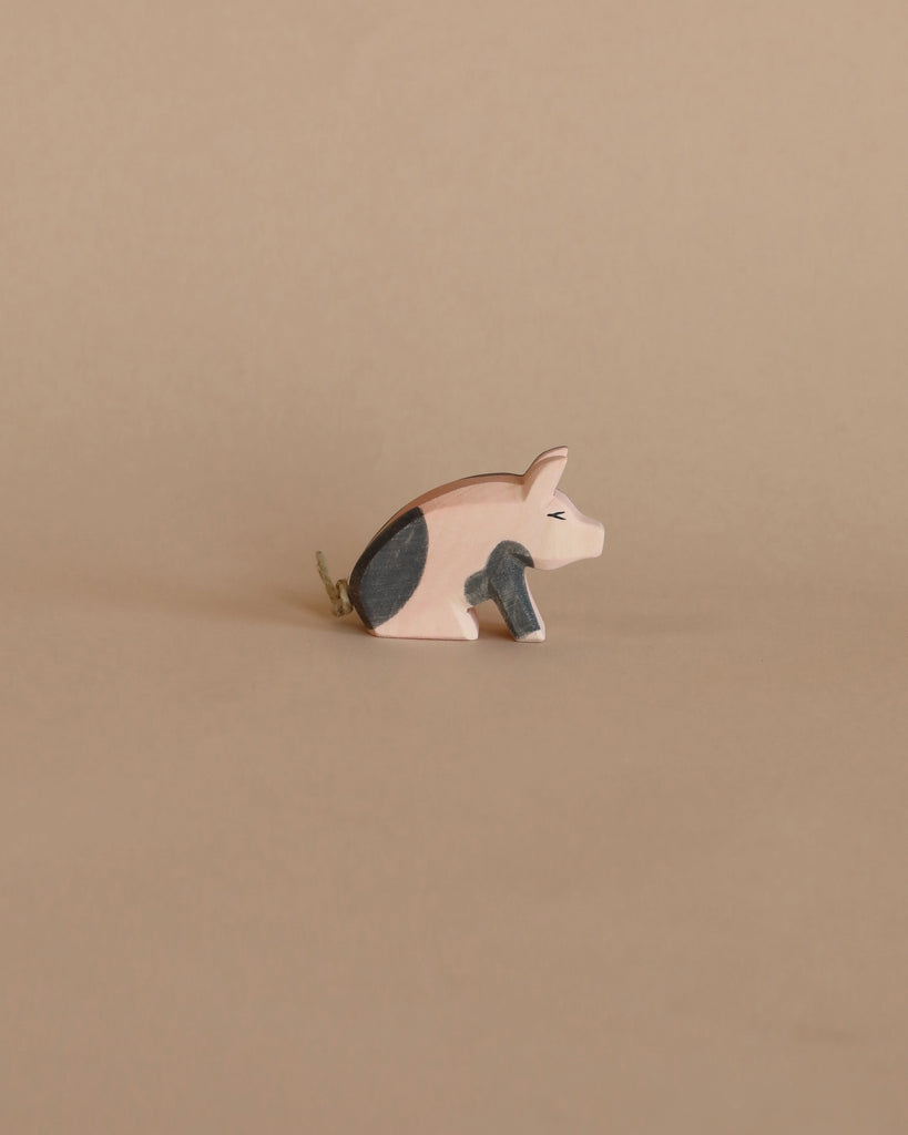 A handcrafted Ostheimer Spotted Piglet - Sitting with black and white painted details, positioned against a plain beige background.
