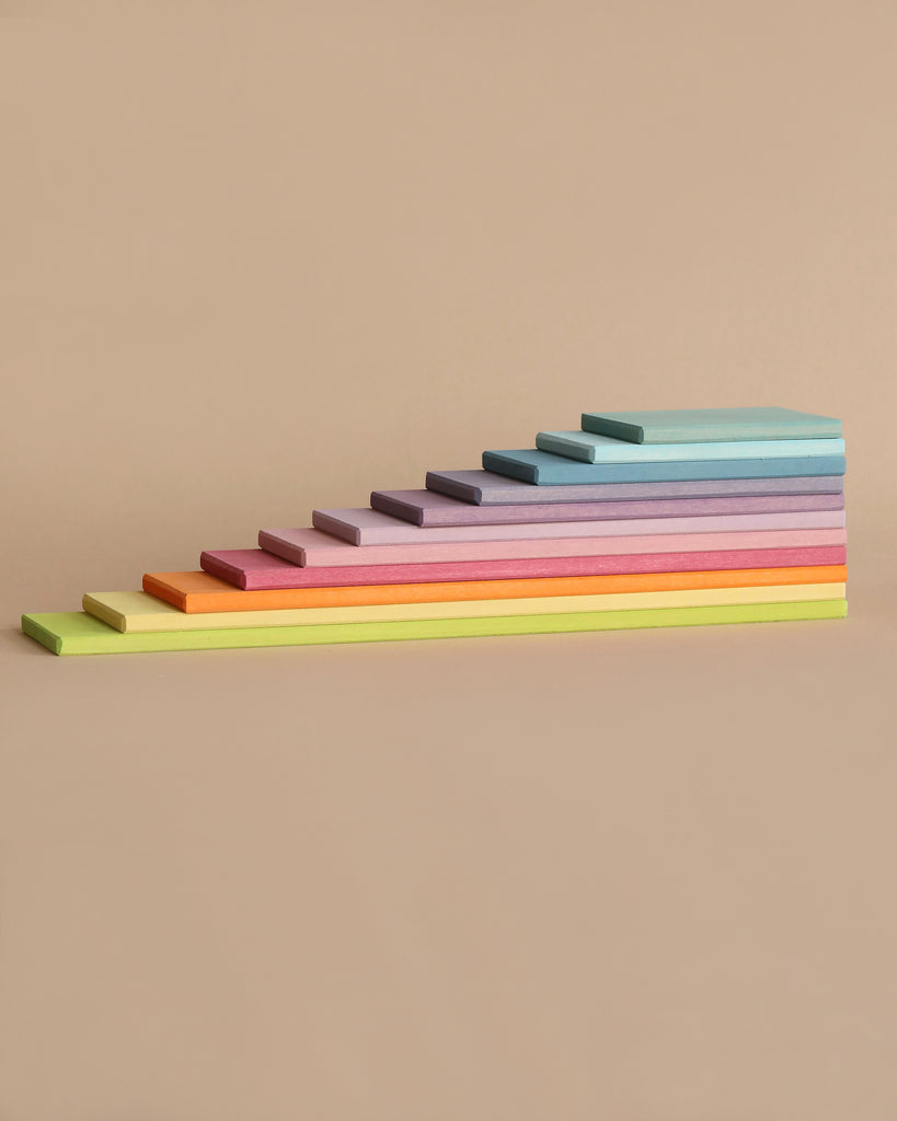 An arrangement of rectangular, colorful sticky notes in varying sizes, stacked in an ascending order from left to right, reminiscent of the Grimm's Pastel Building Boards Set. The colors include yellow, orange, pink, purple, blue, and green against a plain beige background.