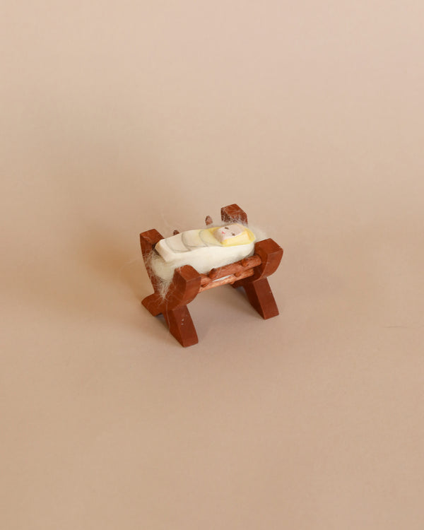 A small wooden stool with an intricate design carries an Ostheimer Baby In Crib partially wrapped in what appears to be a web or light gauze, set against a plain beige background. This piece is reminiscent of the Ostheimer Baby In Crib.