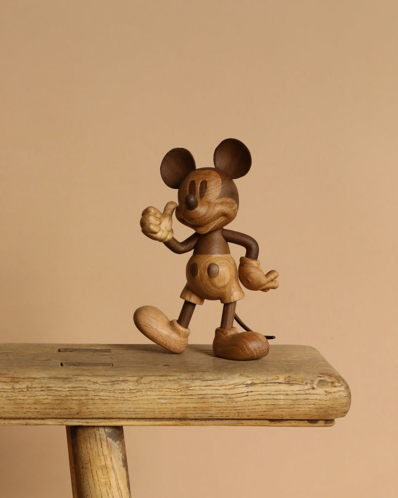 The Mickey Mouse, Oak figurine, featuring classic round ears and gloves, is posed on a wooden surface against a plain background.