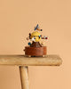 The Space Exploration Music Box by Wooderful Life, with a yellow and blue figure and wooden details, is displayed on a rustic bench against a simple beige background.