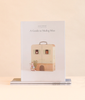 Odin Parker’s Maileg Catalog featuring an illustration of a toy mouse on a scooter in front of a suitcase house in this miniature world.
