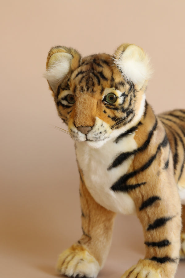 A realistic Tiger Cub - Standing plush toy with detailed fur patterns and expressive eyes, standing against a soft beige background.