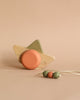 A Handmade Wooden Boat Pull Toy, crafted from solid wood with a green tail and orange wings, is placed on a beige background, next to a string of green and orange beads.