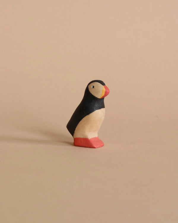 A small Handmade Wooden Puffin, painted with non-toxic paint in black, white, and red, stands upright against a plain beige background.