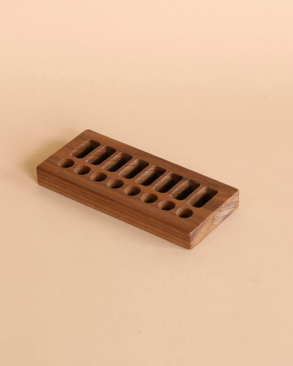 A Wooden Crayon Holder 8 Stick / 8 Block with multiple round holes, set on a plain beige background. The rack is rectangular and made of sustainably sourced walnut wood.