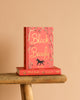 A red hardcover "Black Beauty | Collector's Edition" stands upright on a wooden bench, another copy laid flat beneath. The cover features gold lettering, floral motifs, and a galloping horse silhouette.