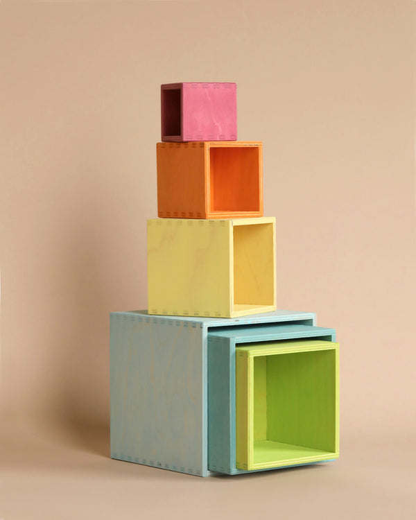 A stack of colorful, non-toxic Grimm's Large Pastel Set of Boxes of varying sizes against a beige background. The versatile toy is open and nested inside each other, creating a gradient effect from pink at the top to green and blue at the bottom. Perfect for children to stack and sort creatively!