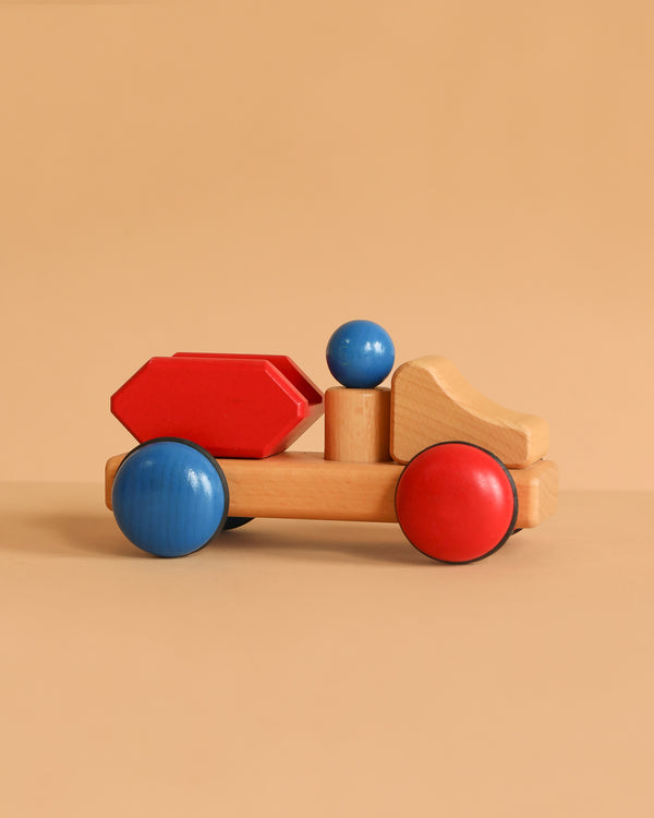 The Fagus Wooden Skip Truck - Mini Series features blue and red wheels, a natural wood cab, a red cargo section, and comes with a removable peg figure for construction play—all set against a plain beige background.