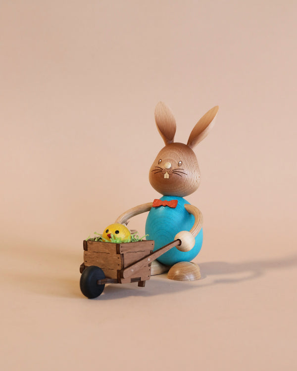 A Collectible Dregeno Easter Figure - Rabbit with Wheelbarrow, pushing a cart filled with yellow chicks on a light beige background.