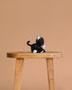 The Olli Ella Binky Kitten Koko - Black is a small black and white plush cat toy, shown sitting on a wooden stool against a light brown background—ideal for cuddling.