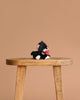 The Olli Ella Binky Kitten Kit - Black & White, a plush toy holding a red heart, sits on a wooden stool against a plain beige background.