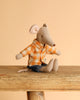 Perched on a wooden surface, the charming Dad Mouse toy from Maileg wears a yellow shirt with denim shorts against a soft beige backdrop.