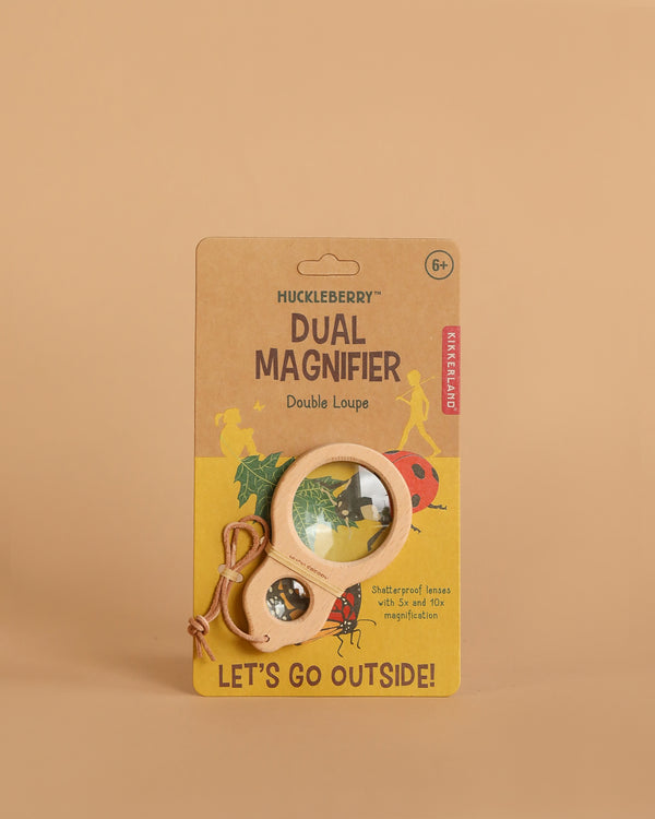 A packaged Huckleberry Dual Magnifier for ages 6+, with a wooden frame, shatterproof 10x lens, and string, is displayed on a tan background. The package says "LET'S GO OUTSIDE!" and features outdoor-themed illustrations.
