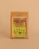 The Huckleberry Pressed Flower Frame kit, in green and brown packaging with floral and nature-themed illustrations, includes a beechwood frame and is displayed on a plain beige background.