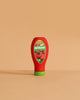 The Erzi Ketchup Pretend Food is a realistic toy bottle with a green cap, standing upright on a beige surface. Non-toxic and ideal for store or kitchen play, it features a tomato label reading "Bio Ketchup.
