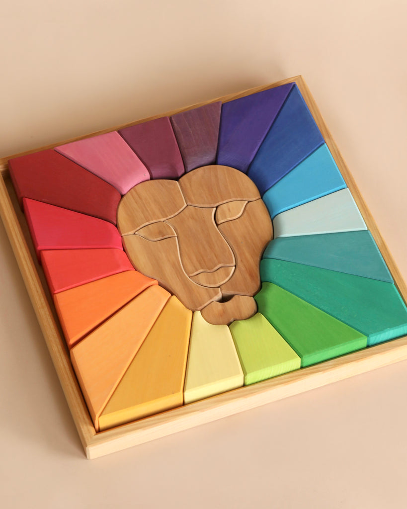 A Grimm's Rainbow Lion Building Set forms a lion's face in the center, surrounded by colorful geometric shapes in shades of purple, blue, green, yellow, and red, arranged in a square natural wood frame.