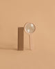 The Wood Magnifier, featuring a beechwood frame, stands upright beside a wooden rectangular block on a simple beige surface with a matching beige background.