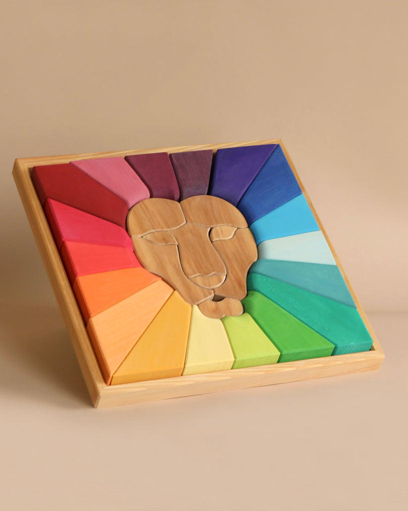 A Grimm's Rainbow Lion Building Set featuring a lion's face in the center. Surrounding the lion's head are colorful geometric shapes arranged in a radial pattern, painted in vibrant gradient colors ranging from reds and oranges to blues and greens. The puzzle sits in a natural wood tray.