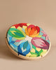 A round, colorful geometric puzzle featuring floral-like patterns with overlapping leaf shapes in various vibrant colors. The wooden Grimm's Lara Circle Flower Building Set challenges spatial thinking skills as you arrange them within a wooden frame, creating a visually appealing artwork against a plain beige background.