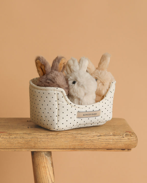 The Konges Sloejd Bunnys in Basket Set features three soft bunnies in brown, white, and beige nestled in a small fabric basket with black polka dots. CE certified for safety and comfort, perfect for little ones.