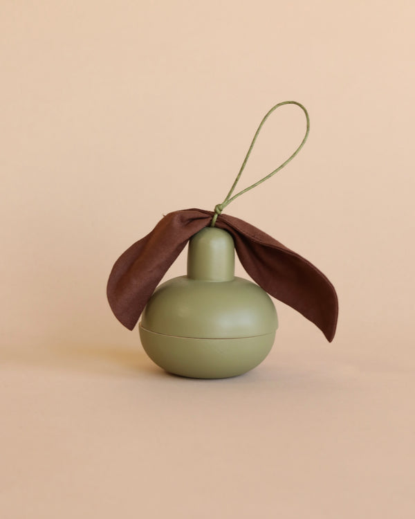 A Wooden Pear & Little Friend features a spherical, olive-green wooden container with a rounded top and a brown fabric ribbon tied around the neck. A looped green string is attached to the top, resembling a small decorative ornament, set against a plain beige background. It could easily be mistaken for an artisanal wooden fruit.