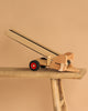 The Fagus Wooden Conveyor Belt, featuring "fagus" on its side and red and black wheels, sits angled upward on a rustic wooden bench against a beige background. It's part of the Fagus vehicles line.