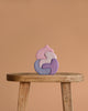 Grimm's Casa Coral Building Blocks, a pastel-colored, abstract wooden puzzle made from handpainted wood, sits on a rustic wooden stool against a plain light brown background.