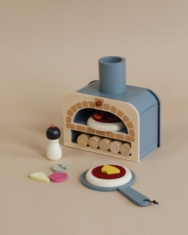 A children's Wooden Make Me A Pizza Set, including a pizza oven, some detachable burners, and wooden play food like a pizza slice with various toppings and an egg, on a soft beige background.