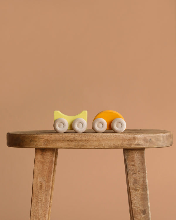 A small, minimalist Grimm's Stacking Car - Yellow sits on a rustic wooden stool against a plain beige background, ideal for imaginative color matching play.