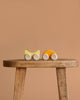 A small, minimalist Grimm's Stacking Car - Yellow sits on a rustic wooden stool against a plain beige background, ideal for imaginative color matching play.