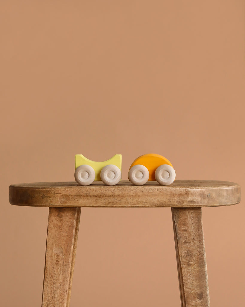 A small, minimalist Grimm's Stacking Car - Yellow sits on a rustic wooden stool against a plain beige background, ideal for imaginative color matching play.