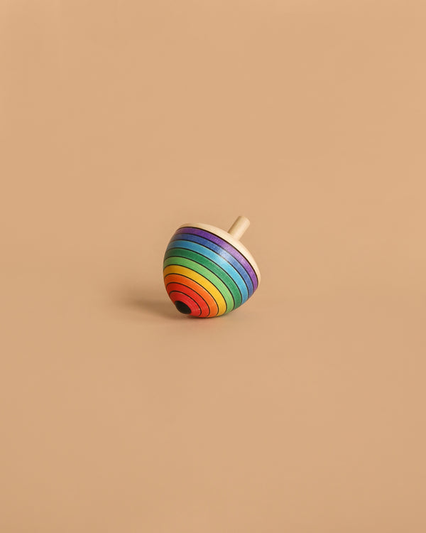 The Mader Rainbow Egg Spinning Top - Purple, crafted from maple wood in Austria, features vibrant stripes and is displayed on a plain beige surface.