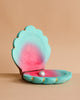 The Bumbu Handmade Wooden Big Shell with Pearl is a turquoise and pink, clam-shaped hinged box, open to display a single silver pearl inside. Handcrafted to evoke marine life, it is set against a plain light beige background.