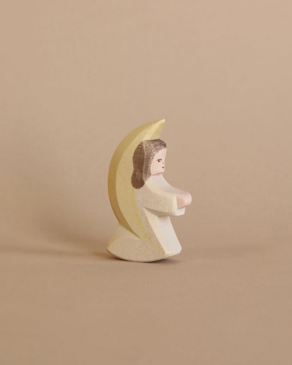 A small handcrafted Ostheimer Little Angel - Off-White figurine wrapped in a yellow crescent moon cape, against a plain beige background.