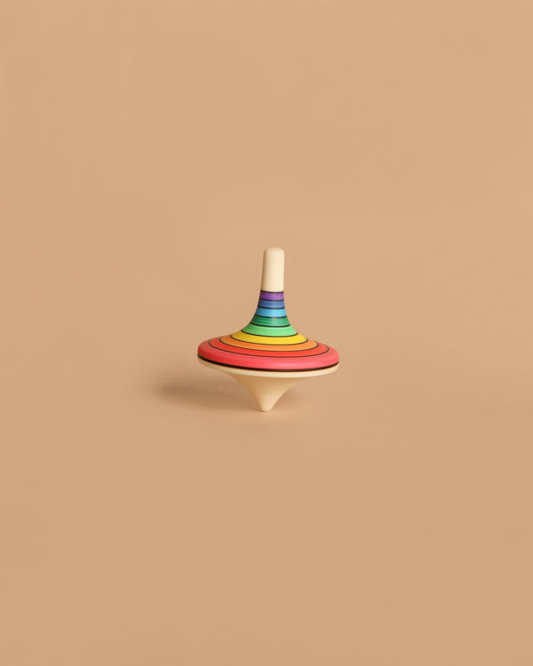 The Mader Rallye Rainbow Spinning Top, Small - Red features vibrant concentric stripes and stands upright on a beige background, making it a delightful toy for 3-year-olds.